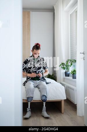 Portrait of disabled young man sitting in bed indoors at home, leg prosthetic concept. Stock Photo