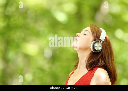 Profile of a relaxed woman listening to music with wireless headphones breathing fresh air in a forest Stock Photo