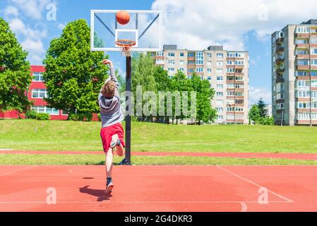 Attractive young boy shooting ball to the hoop at playground.cute young boy plays basketball on the playground in the summer warm day. Stock Photo