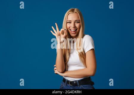 Blonde young happy woman smiling and showing ok sign isolated over blue background Stock Photo