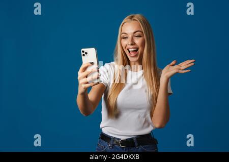 Excited woman holding copyspace while taking selfie on cellphone isolated over blue background Stock Photo