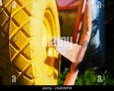 Selective close-up focus on tread of yellow rubber wheel of garden cart illuminated by bright sunlight on blurred background Stock Photo