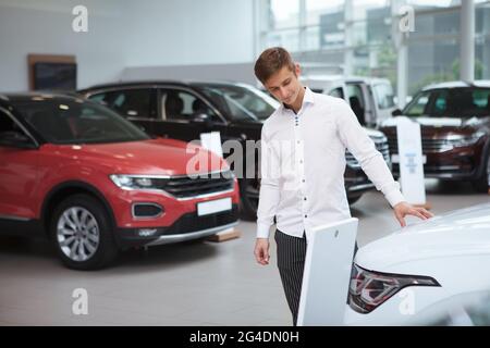 Handsome young businessman choosing new car to buy at the dealership, copy space Stock Photo