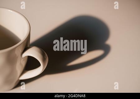 Coffee cup with long shadow cream color side view. Focus on cup. Morning energy Stock Photo