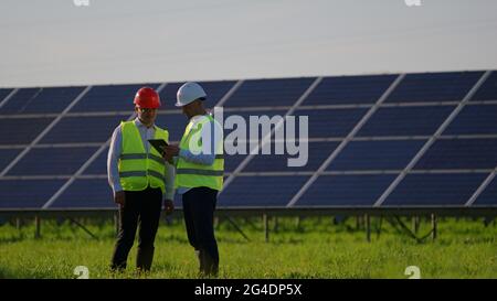 The engineer is greeting his colleagues. They are talking and standing next to solar panels Stock Photo