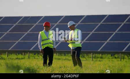The engineer is greeting his colleagues. They are talking and standing next to solar panels Stock Photo