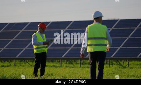 The engineer is greeting his colleagues. They are talking and standing next to solar panels Stock Photo