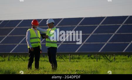 The engineer is greeting his colleagues. They are talking and standing next to solar panels Stock Photo