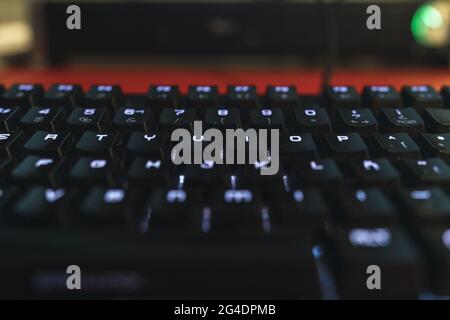 Closeup of the middle part of a black keyboard with white rgb lights on red table Stock Photo