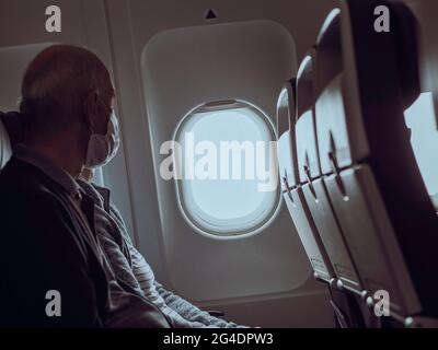 A couple of travelers sit at an airplane window. The mask wearing couple sit at a sunny window sleeping and looking at the view out of the window. Stock Photo