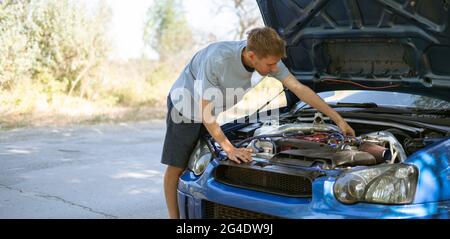 young man standing near the car with opened hood and fix some problems with engine Stock Photo