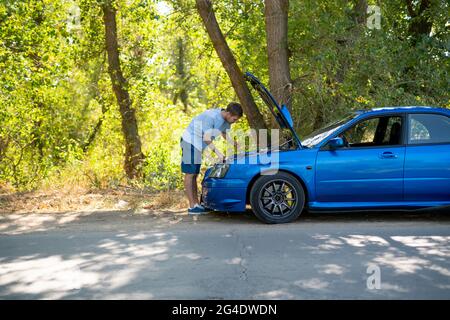 young man standing near the car with opened hood and fix some problems with engine Stock Photo