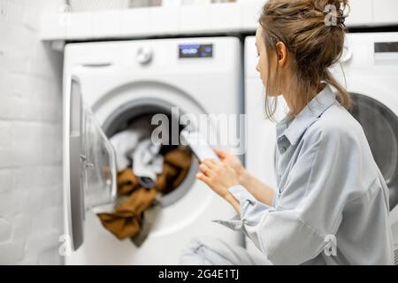 Woman controls washing machine with a smartphone Stock Photo