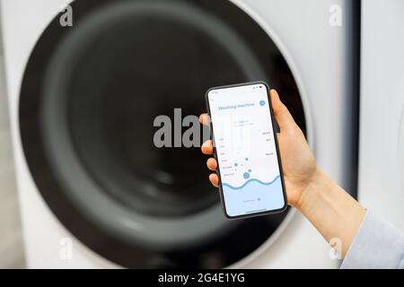 Woman controls washing machine with a smartphone Stock Photo
