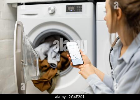 Woman controls washing machine with a smartphone Stock Photo