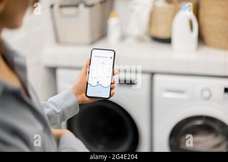 Woman controls washing machine with a smartphone Stock Photo