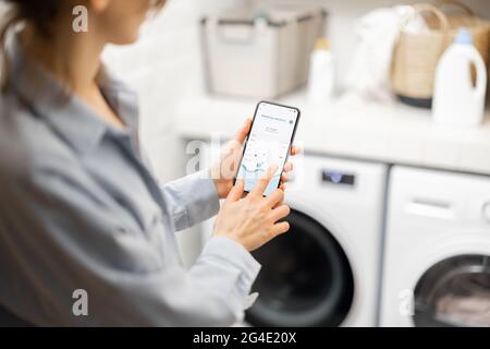 Woman controls washing machine with a smartphone Stock Photo