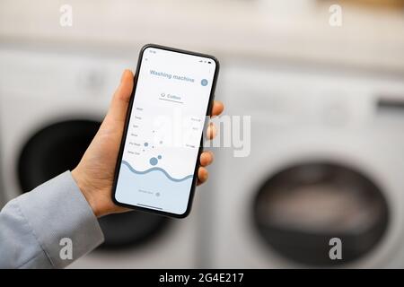 Woman controls washing machine with a smartphone Stock Photo