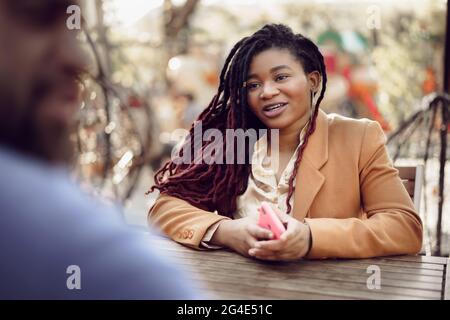 Smiling young african woman sitting at a table in cafe with caucasian man and having a talk Stock Photo