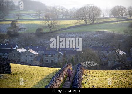 A woman wrapped up warm in pink coat and yellow bobble hat takes a winter walk near the Linton Falls near the village of Grassington in the Yorkshire Stock Photo