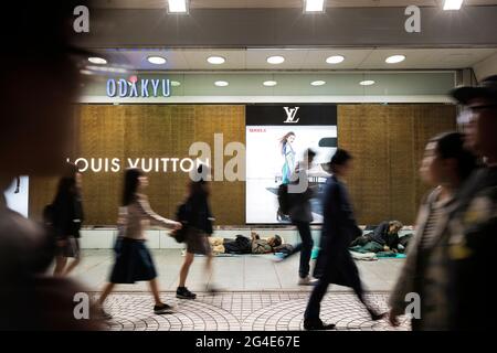 Commuters walking past homeless people sleeping outside the Odakyu luxury department store in Shinjuku, Tokyo, Japan Stock Photo