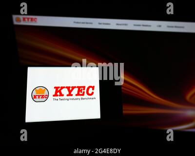 Person holding mobile phone with logo of Taiwanese company King Yuan Electronics Corp. (KYEC) on screen in front of webpage. Focus on phone display. Stock Photo