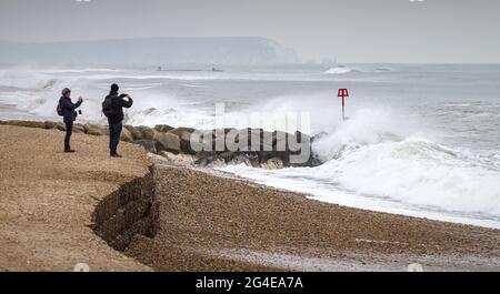 Two, Pair, People Photographing Heavy Waves Crashing Onto Hengistbury Head Beach During A Storm In Winter With Needles And Isle Of Wight In The Distan Stock Photo
