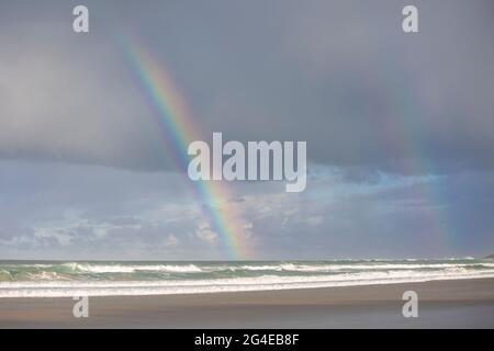 A bright and clear rainbow in a cloudy sky over the sea Stock Photo