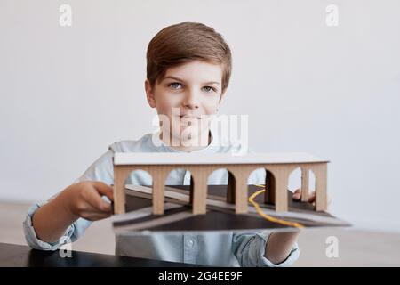 Front view portrait of smiling boy holding cardboard model while working on handcrafted school project, copy space Stock Photo