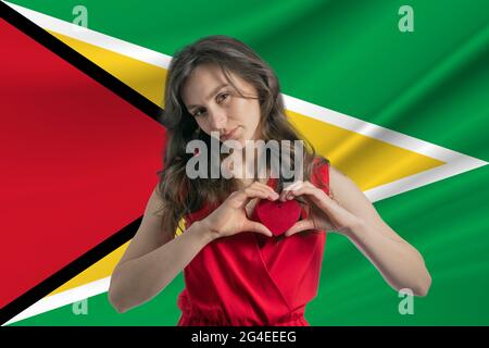 Love Guyana. A girl holds a heart on her chest in her hands against the background of the flag of Guyana. The concept of patriotism. Stock Photo