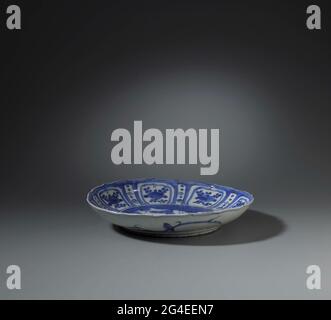 . Scale of porcelain with a scalloped edge, painted in underglaze blue. On the flat four deer in a landscape at rocks and flowering plants, two flying birds and a pine; The wall with eight square, scalloped cartouches with a fruit or flower branch, narrow compartments with dots and a brush between them; The outer wall with twice a bird on an elegantly painted branch. Cracking porcelain in blue and white. Stock Photo