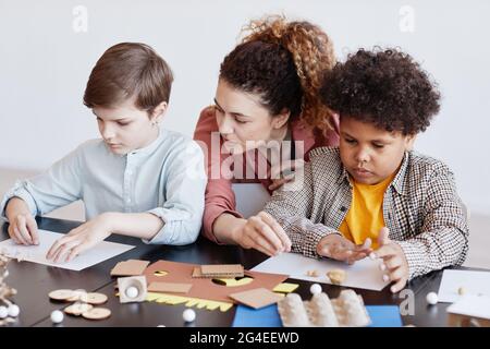 Portrait of two kids making cardboard models during art and craft class in school with female teacher Stock Photo