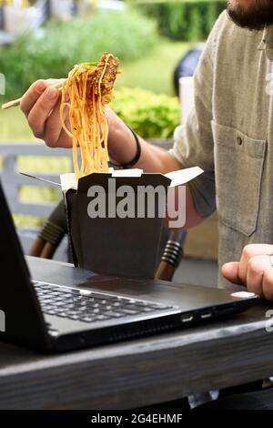 Wok in box in black food container. Holding spicy noodles with chopsticks. Fast food delivery service. Takeaway chinese street meal Stock Photo