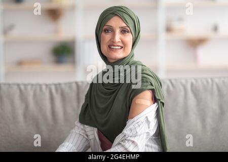 Happy Vaccinated Muslim Woman Showing Arm With Plaster Bandage Indoor Stock Photo