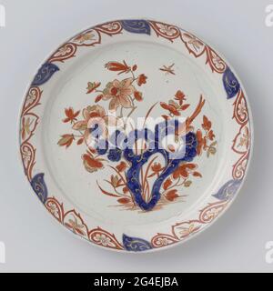 . Round plate of multi-colored padded faience, with a rock with flowers, plants and a bird painted on the flat in the colors red, blue and gold. A palmet edge is painted on the edge. The plate is marked at the rear with the MOTK monogram. Stock Photo