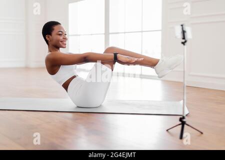 Smiling Black Woman Doing Sit-ups Exercise Looking At Phone Stock Photo