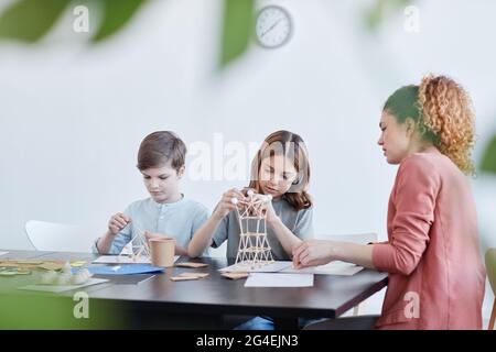 Side view portrait of female teacher helping children making wooden models during art and craft class in school, copy space Stock Photo
