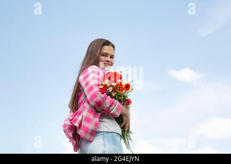 Bouquet of wildflowers: poppies, daisies in hand against the blue sky. flowers in a woman's hand Stock Photo