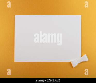 Sheet of paper on gold background with white ribbon. Flat lay horizontal composition with copy space. Creative layout, studio shot. Stock Photo