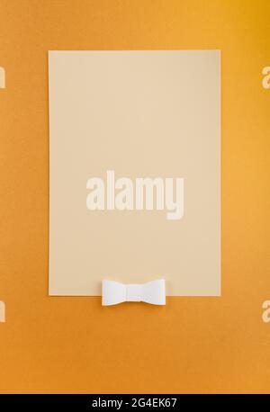 Sheet of paper on gold background with white ribbon. Flat lay vertical composition with copy space. Creative layout, studio shot. Stock Photo