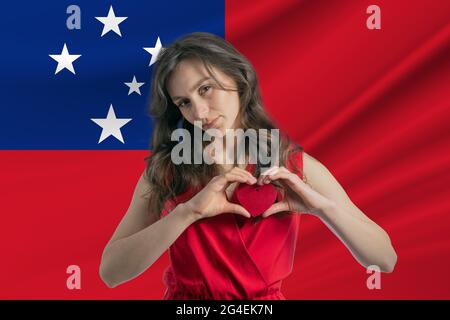 Love Samoa. A girl holds a heart on her chest in her hands against the background of the flag of Samoa. The concept of patriotism. Stock Photo