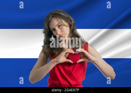 Love El Salvador. A girl holds a heart on her chest in her hands against the background of the flag of El Salvador. The concept of patriotism. Stock Photo
