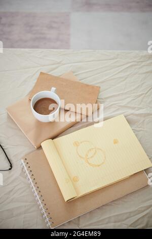 Opened notepad with coffee stains, books, planners and cup with cappuccino on bed Stock Photo