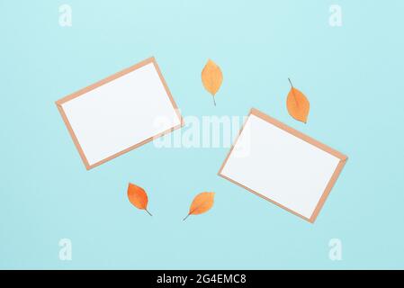 Autumn stationery still life. Blank greeting card mockups with envelopes and dry yellow autumn leaves on a blue paper background. Top view, flat lay