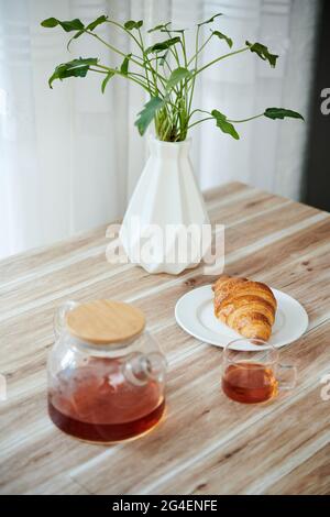 Teapot, cup and fresh croissant on kitchen table served for breakfast Stock Photo