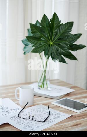 Documents with block schemes, coffee and tablet computer on table decorated with leaves in vase Stock Photo