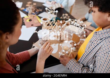 High angle closeup of African-American boy presenting school project to female teacher during art and craft lesson Stock Photo