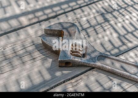 An old and rusty adjustable wrench made of chrome vanadium alloy, close-up, lies on old wooden planks in the shade Stock Photo