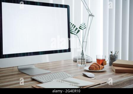 Empty computer monitor, opened planner, croissant on plate and stack of books on desk of university student Stock Photo