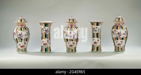 . Five-part cabinet made of porcelain with three baluster vases with lid and two cup cubes with ribbed wall, painted on the glaze in blue, red, pink, green, yellow, purple, black and gold. On the wall cartouches against a common background of vertical tires (harlequin pattern); Two cartouches in the shape of open rolls with a lady (long lijs) with boy (ocean) in a fenced garden with flowering plants, including two leaf-shaped cartouches with ponda branch and butterfly, on either side of the large courses a smaller pomegranate and finger lemon-shaped box with lucky symbols; On the neck a bond w Stock Photo